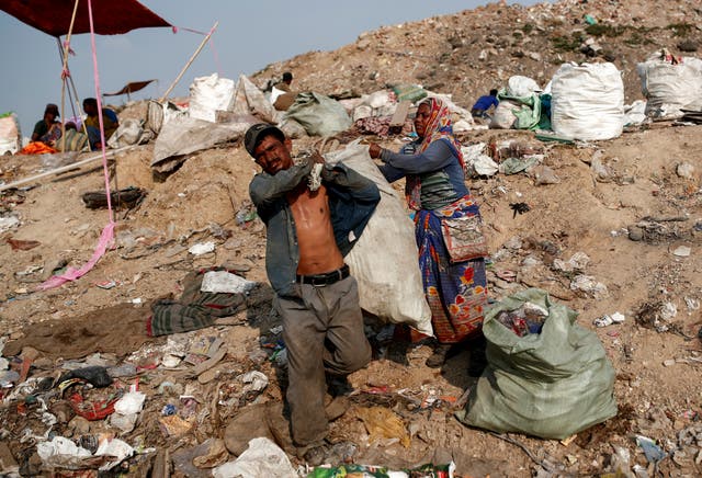 Latifa Bibi helps her husband Mansoor Khan with a sack of recyclable materials that they found at a landfill site
