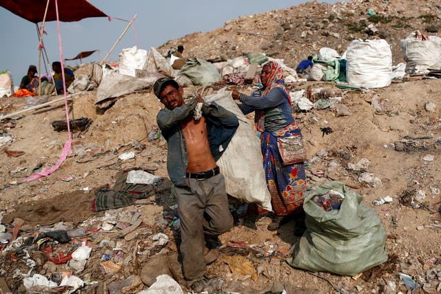 Latifa Bibi helps her husband Mansoor Khan with a sack of recyclable materials that they found at a landfill site