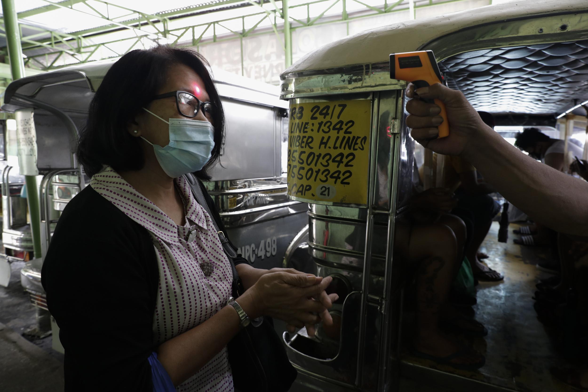 A woman’s temperature is measured before riding a passenger jeepney to help curb the spread of the virus as drivers at the Tandang Sora terminal were recently allowed back on the road after months of not being able to work