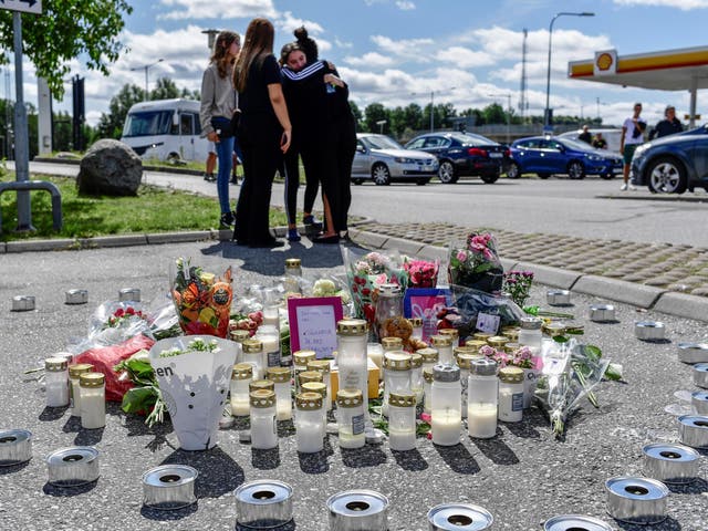 People stand near flowers and candles that have been left at the site where a 12-year-old girl was shot dead in Botkyrka, near Stockholm, Sweden.