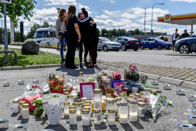 People stand near flowers and candles that have been left at the site where a 12-year-old girl was shot dead in Botkyrka, near Stockholm, Sweden.