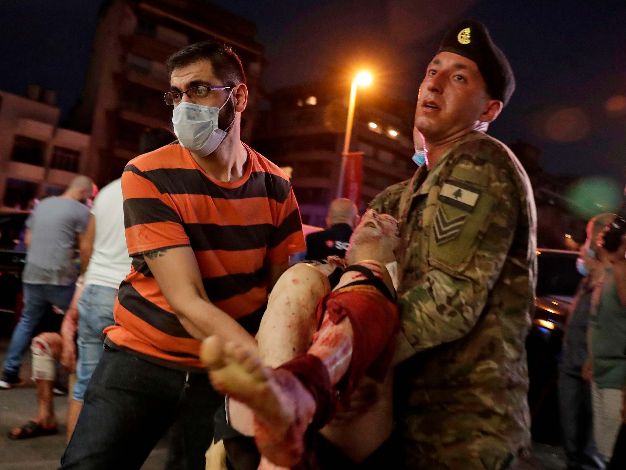 A Lebanese army soldier and a man carry away an injured man at a hospital in the aftermath of an explosion