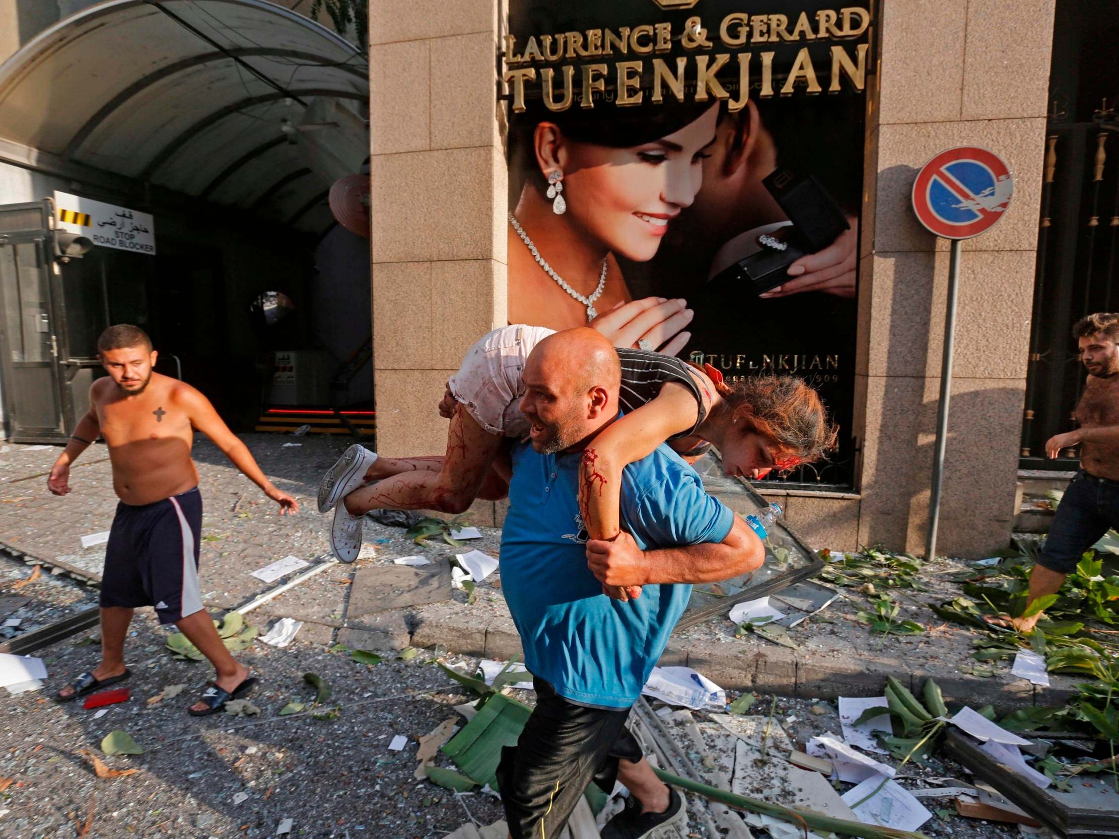 A man carries away an injured girl while walking through debris past in the Achrafiyeh district