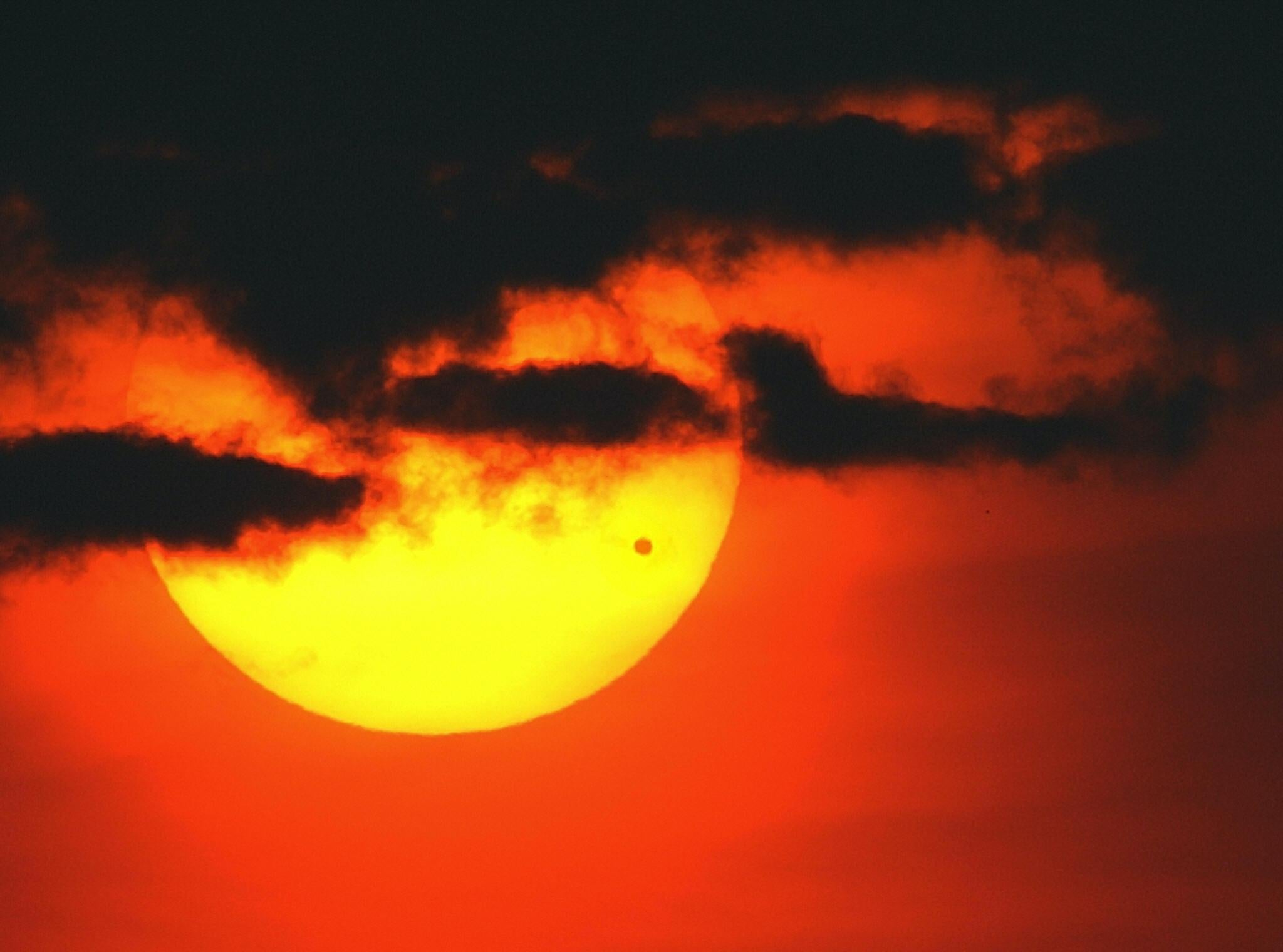 The sun rises through a bank of clouds over the East River of Manhattan as the planet Venus (dot on lower right of sun) crosses its face, 08 June, 2004, in New York