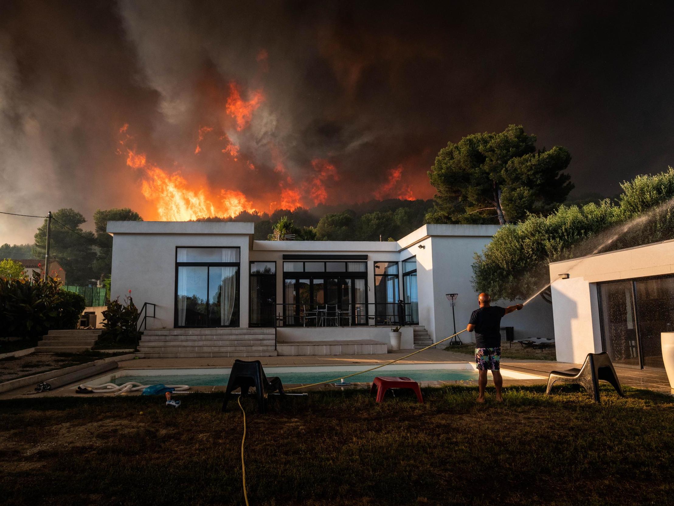 A man uses a garden hose to drench his house before being evacuated as a wild fire burns in the background, in La Couronne, near Marseille
