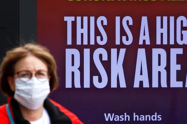A woman wearing a protective mask walks past a warning sign in Manchester