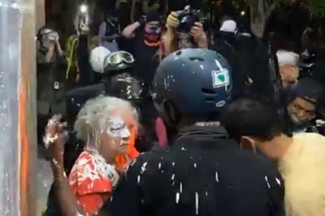 A woman stands in front of a crowd of protesters after they allegedly threw white paint on her