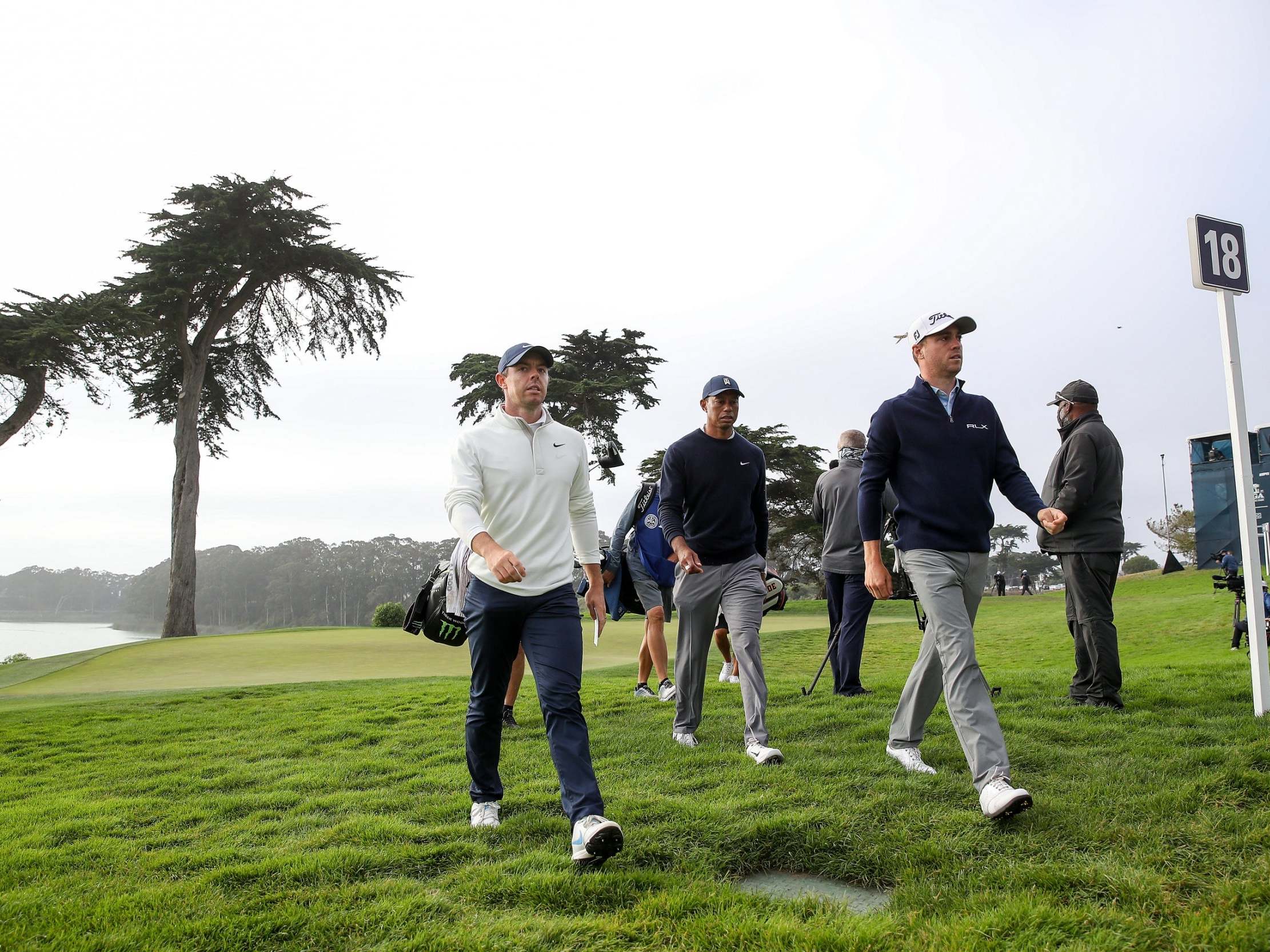 Rory McIlroy marches off the 18th green alongside Justin Thomas and Tiger Woods