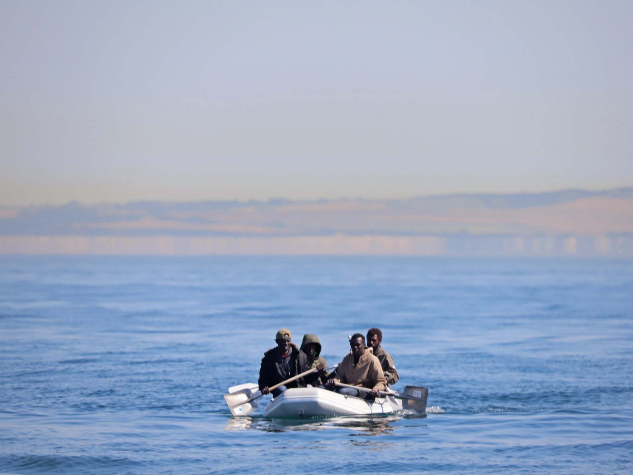 Four men off the coast of France, some using shovels as paddles, use a small dinghy to cross the English Channel on 7 August 2020