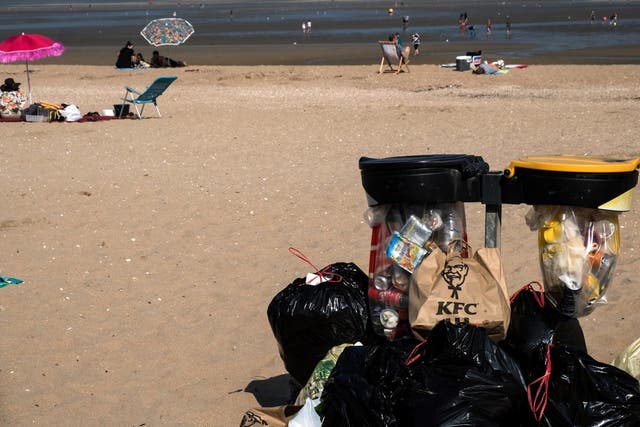 People enjoy the beach, next to a mountain of trash placed next to a bin, in Houlgate, northwestern France