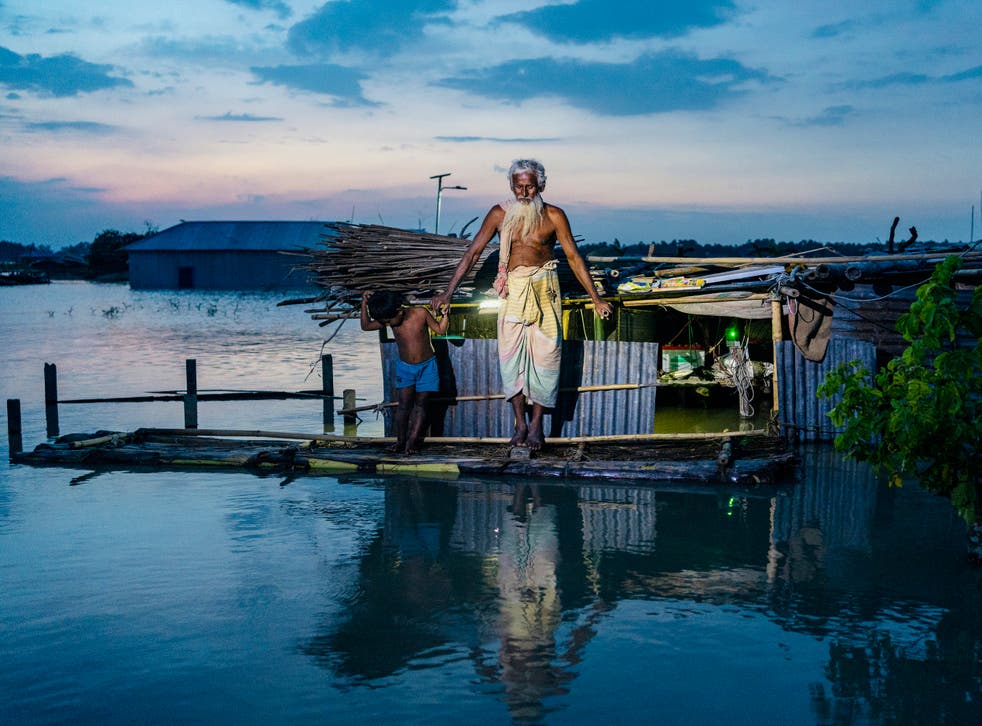 Abdus Samad Sarker and his grandson stand on a raft made from banana trees, in front of Abdus's submerged house