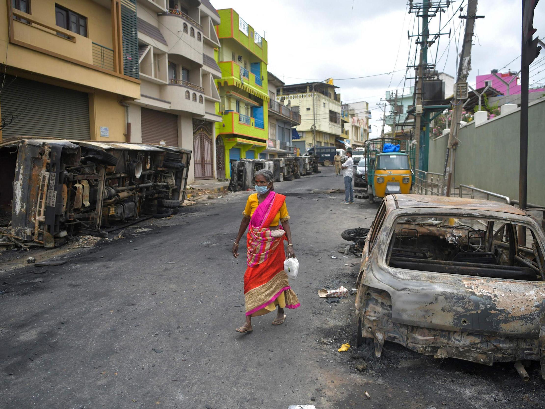A resident walks past the burned-out remains of a car following protests in the city of Bengaluru, India, over a Facebook post about the Prophet Mohammed.
