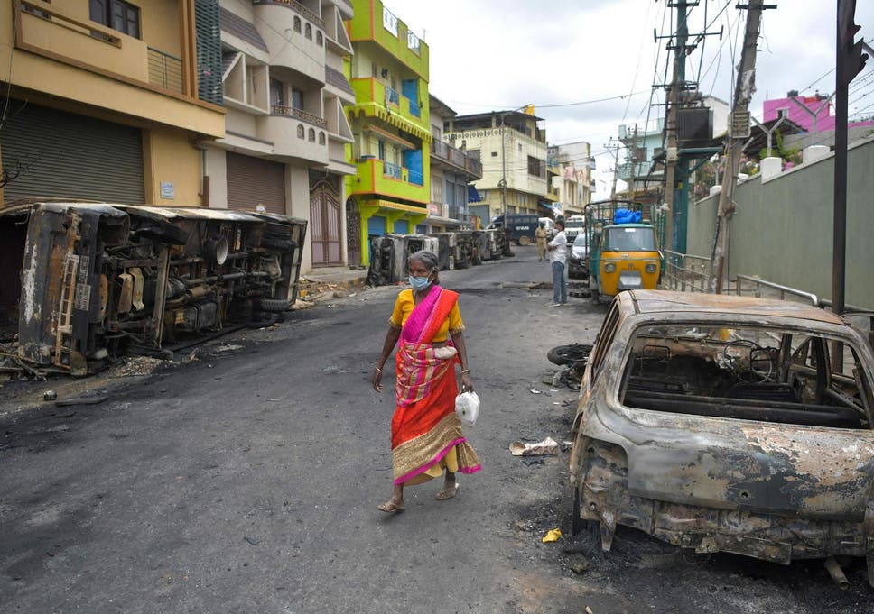 A resident walks past the burned-out remains of a car following protests in the city of Bengaluru, India, over a Facebook post about the Prophet Mohammed. 