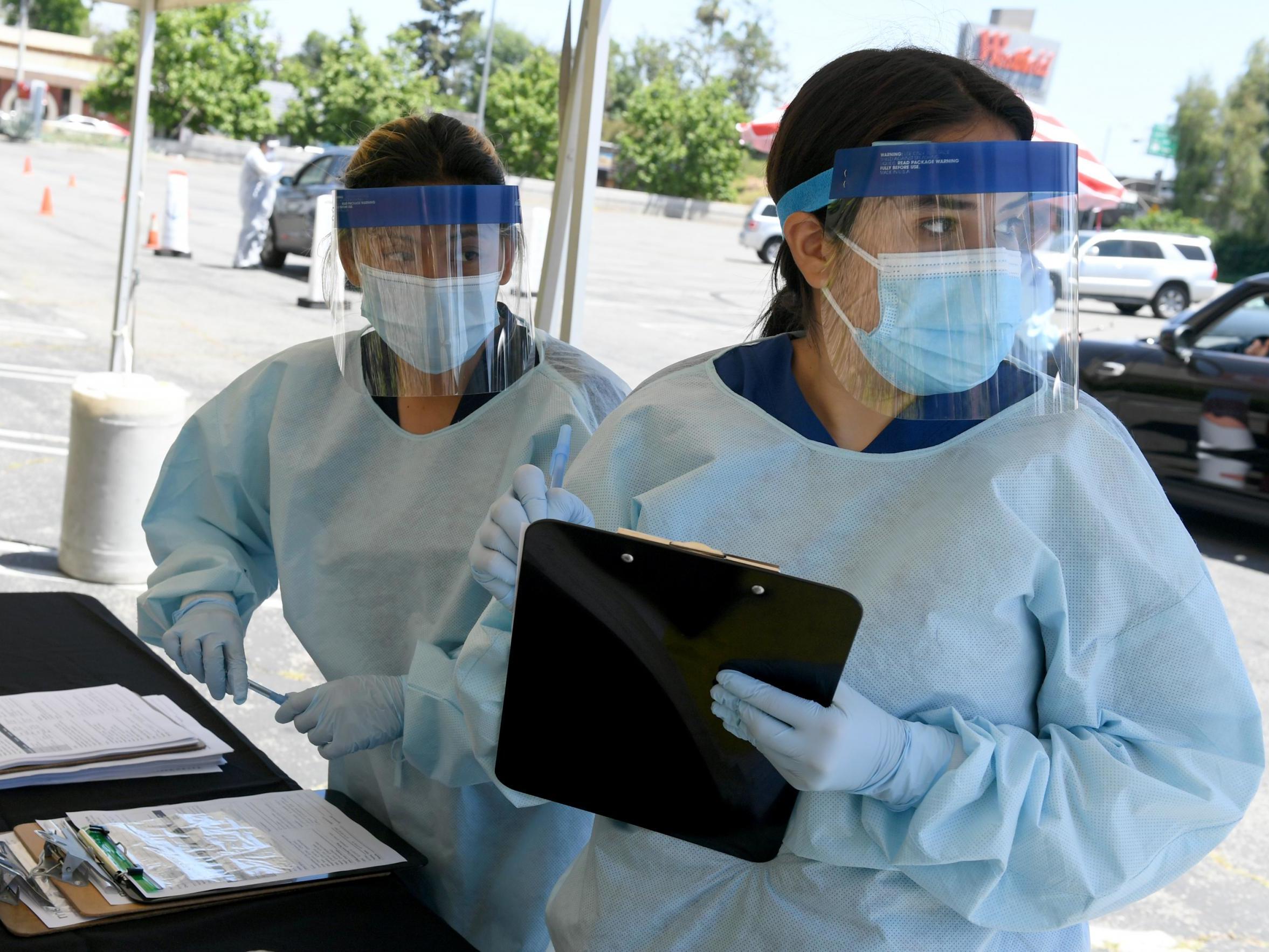 Workers wearing personal protective equipment (PPE) perform drive-up Covid-19 testing administered from a car at Mend Urgent Care testing site for coronavirus at the Westfield Fashion Square on 13 May 2020 in the Sherman Oaks neighbourhood of Los Angeles, California