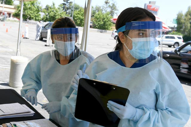 Workers wearing personal protective equipment (PPE) perform drive-up Covid-19 testing administered from a car at Mend Urgent Care testing site for coronavirus at the Westfield Fashion Square on 13 May 2020 in the Sherman Oaks neighbourhood of Los Angeles, California