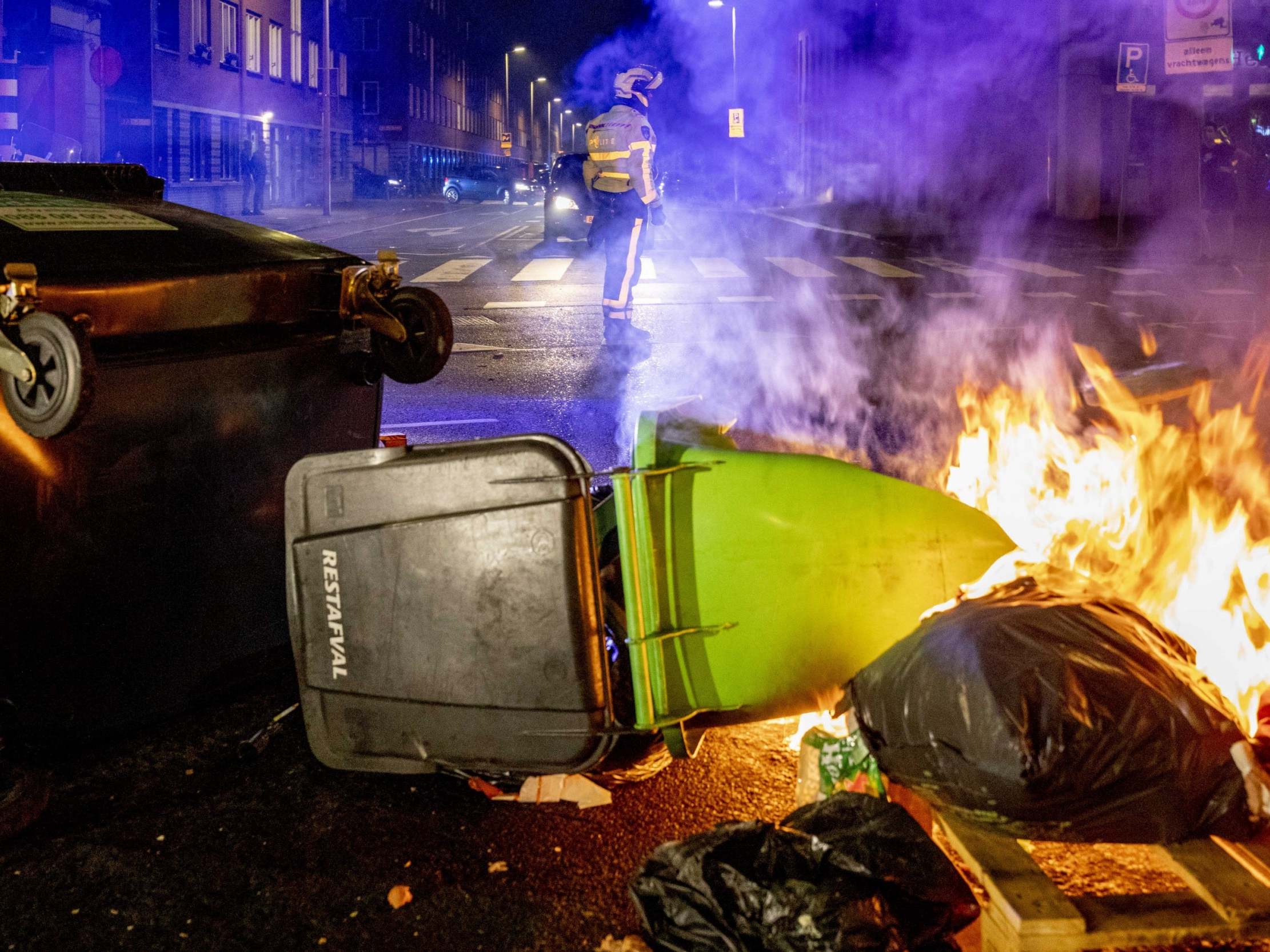 A view of a burning dumpster and other waste containers as a police officer keeps watch in the Schilderswijk neighborhood in The Hague, the Netherlands