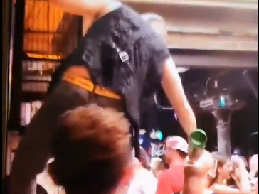 A man standing on the bar pours drinks directly into customer's mouths during the party