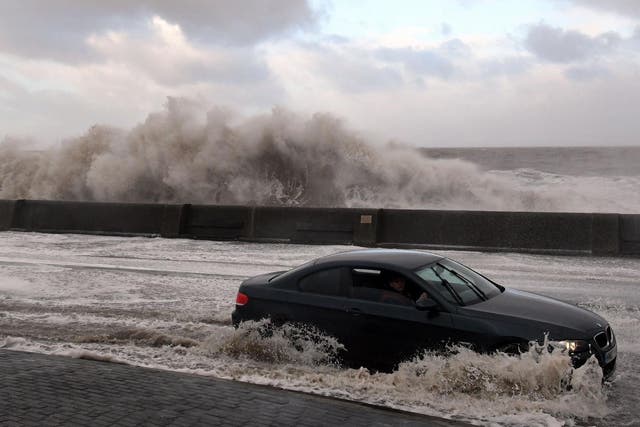 Waves crash over the tidal wall as a motorist travels along the coastal road in New Brighton