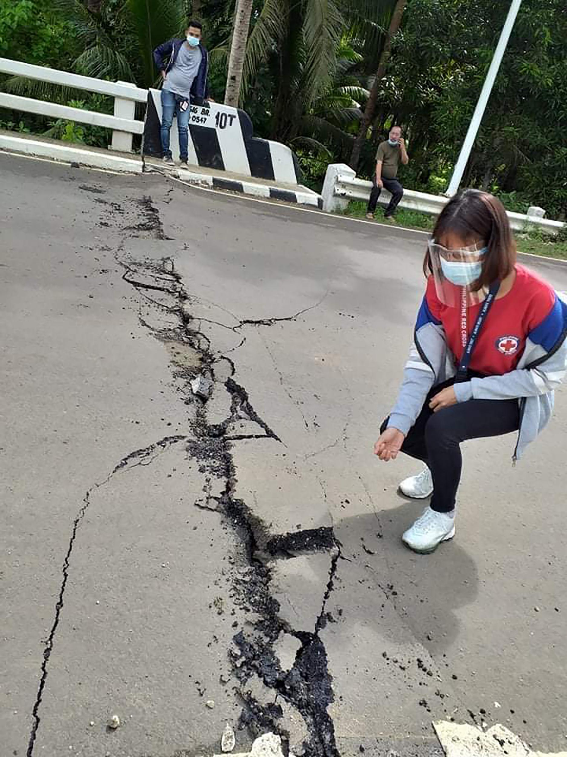 A volunteer looks at the cracks on a road in Cataingan after the quake struck