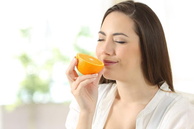 Woman smelling half orange sitting on a couch in the living room at home