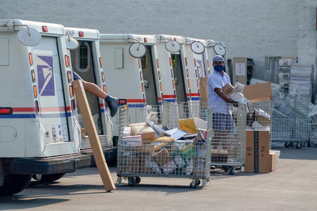 Trabajadores postales clasifican, cargan y entregan correos mientras manifestantes realizan una manifestación para "Salvar a la oficina de correos" fuera de una central del Servicio Postal de los Estados Unidos en Los Ángeles, California, el 22 de agosto de 2020.