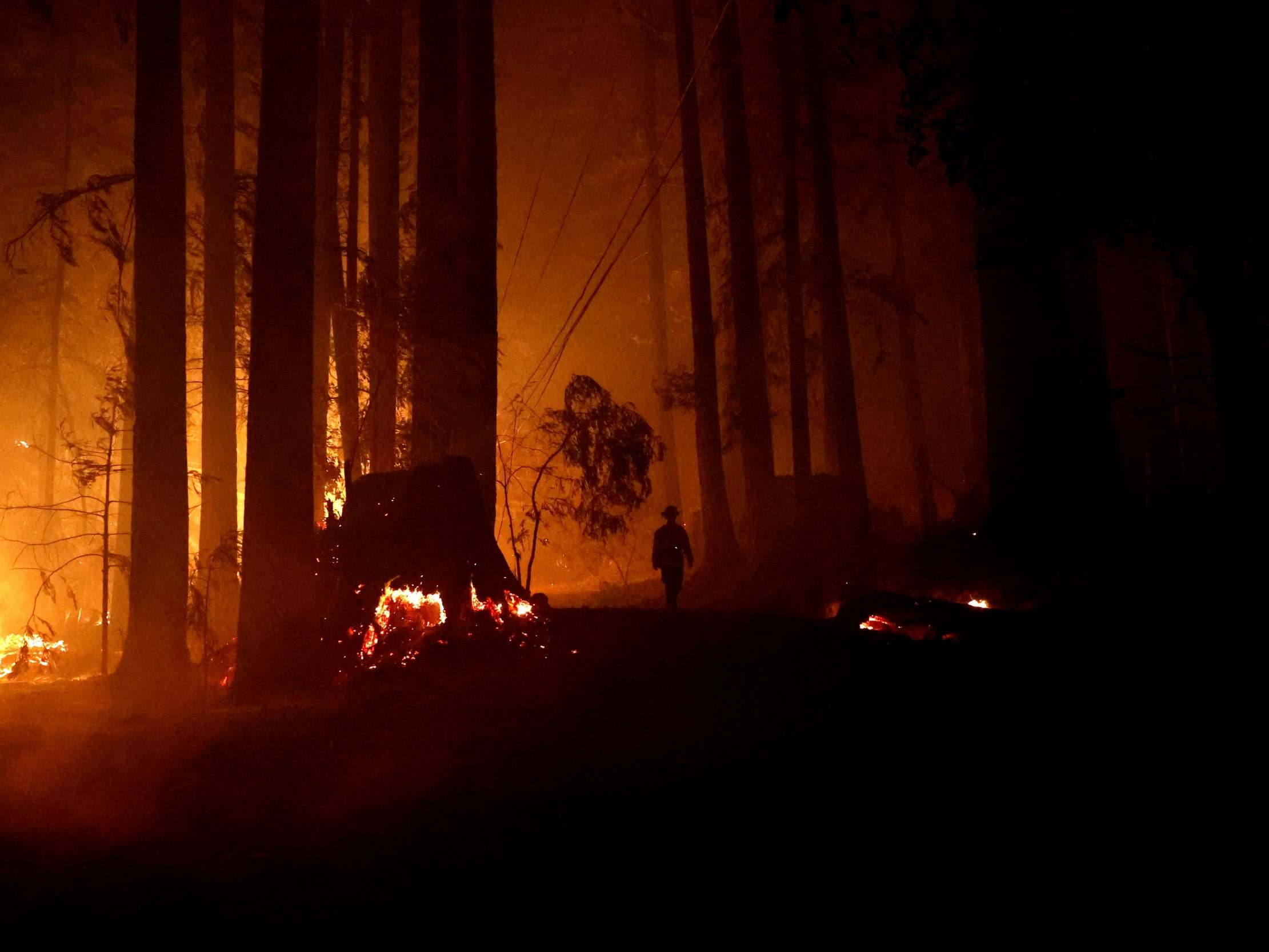 A firefighter walks along a road with fire on both sides during the CZU Lightning Complex Fire in Boulder Creek, California on Friday