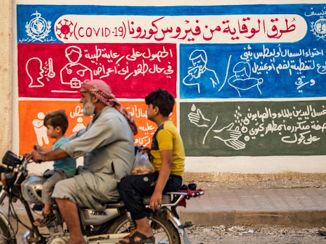 Syrian people ride a motorbike past a mural painted as part of an awareness campaign by Unicef and the WHO bearing instructions on protection from Covid-19