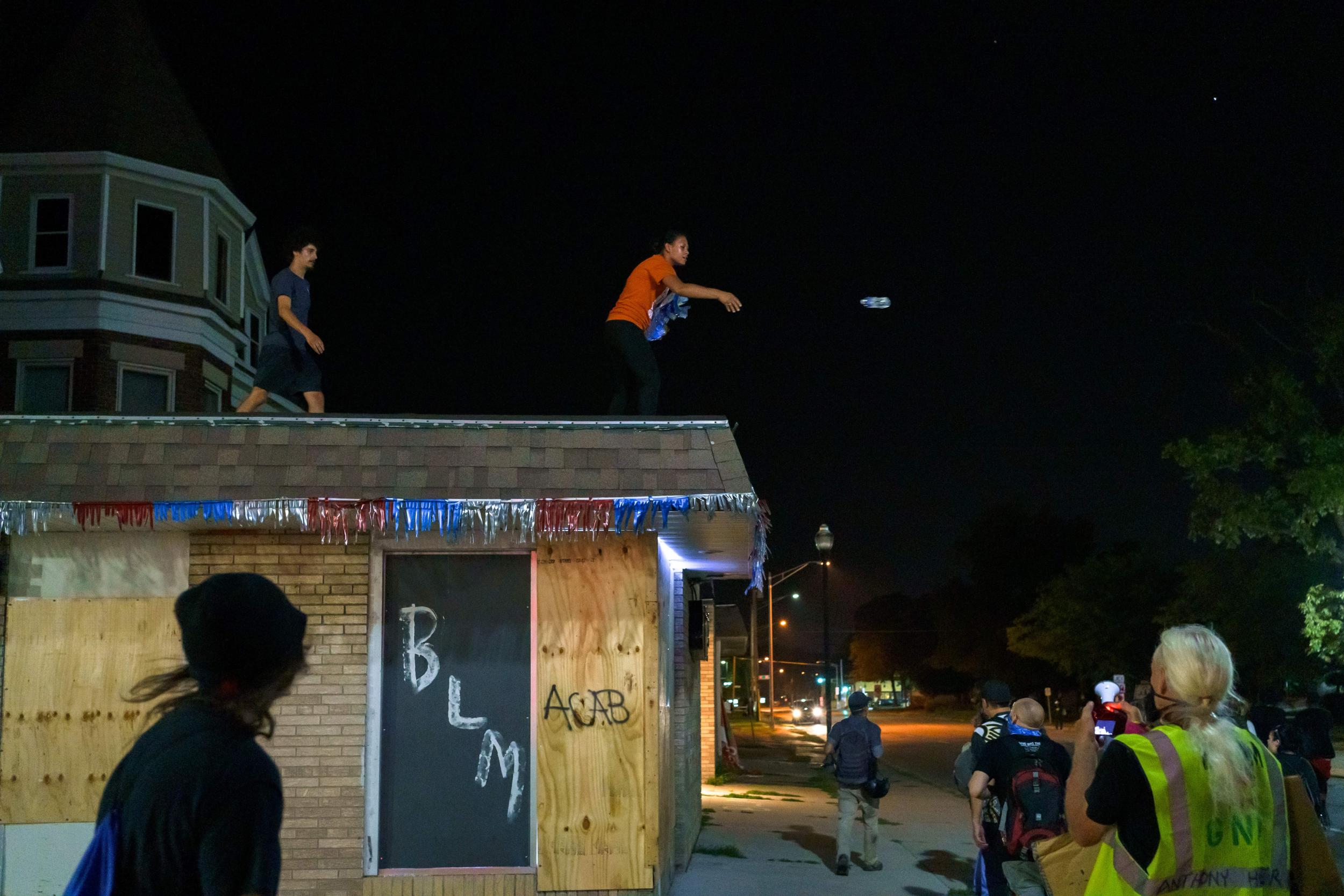 A woman gives bottles of water, from the top of a boarded up house in Kenosha, to protesters after two people were shot dead and a third injured on 25 August, as anti-police protesters clashed with armed vigilante groups during a third night of demonstrations over the police shooting of Jacob Blake