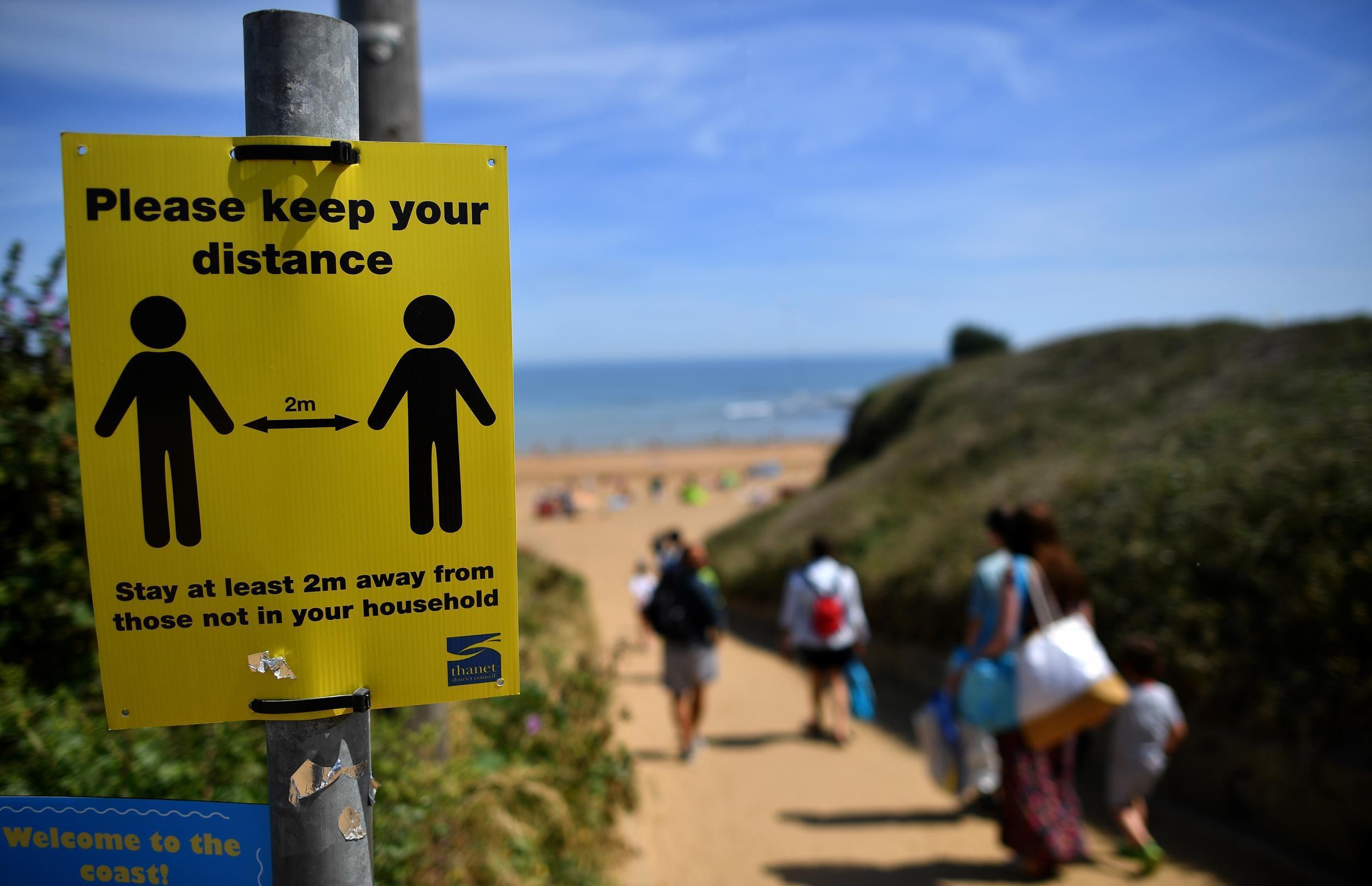 Beachgoers pass a sign advising social distancing as they arrive to enjoy the sunshine on the beach and in the sea at Botany Bay, near Margate (Getty)