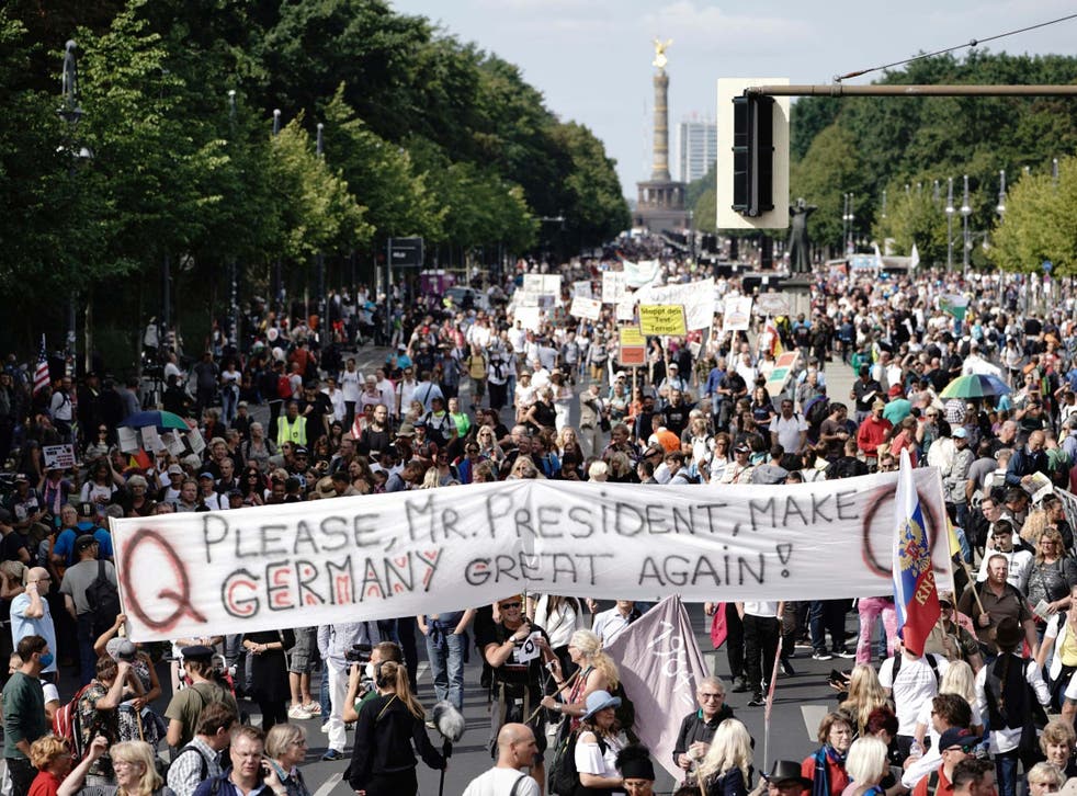 Protesters hold a banner marked with the symbol of the QAnon conspiracy during a mass rally against coronavirus restrictions in Berlin