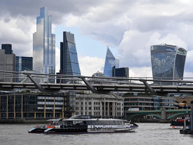 An Uber boat operated in partnership with Thames Clippers, travels along the River Thames as it passes under the Millennium Bridge, backdropped by the skyscrapers of the City of London on 3 August 2020.