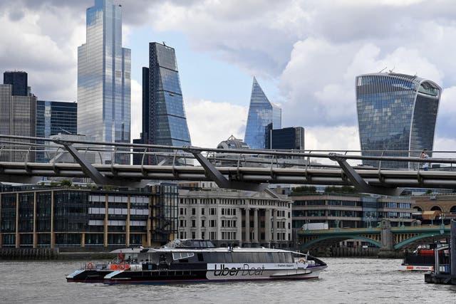 An Uber boat operated in partnership with Thames Clippers, travels along the River Thames as it passes under the Millennium Bridge, backdropped by the skyscrapers of the City of London on 3 August 2020.