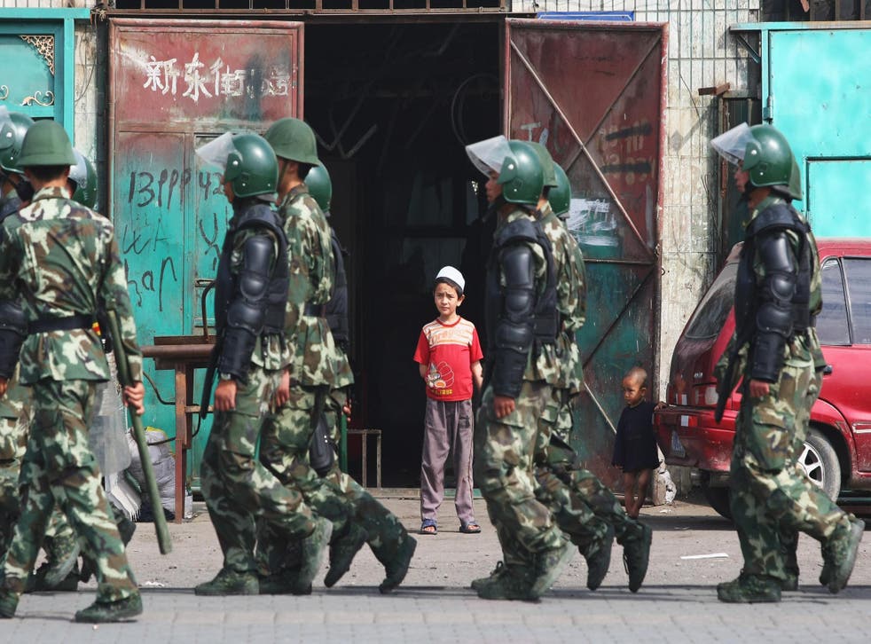 Uighur children watch as police officers pass their home in Urumqi, the capital of Xinjiang