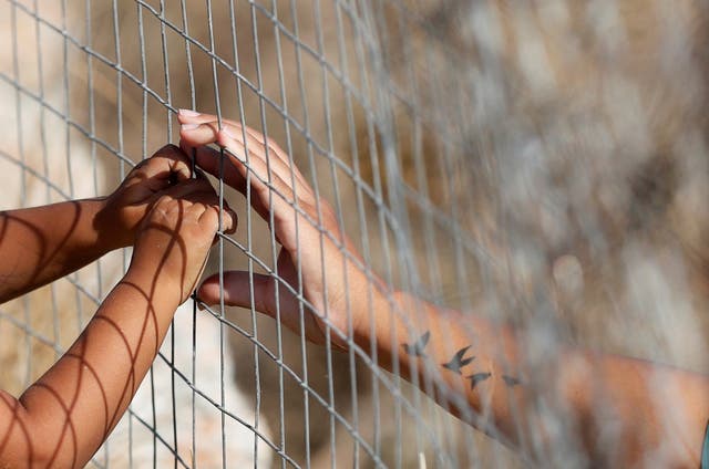 <p>A woman touches hands of a child through a fence at a new temporary camp for migrants and refugees, on the Greek island of Lesbos</p>